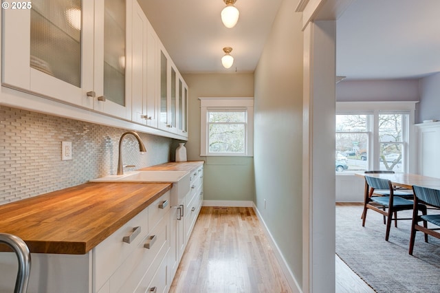 kitchen with a sink, wood counters, white cabinetry, light wood finished floors, and decorative backsplash