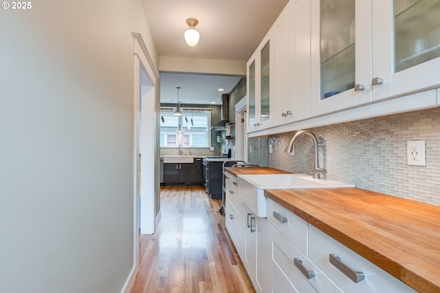 kitchen with tasteful backsplash, wall chimney range hood, light wood-style floors, white cabinets, and a sink