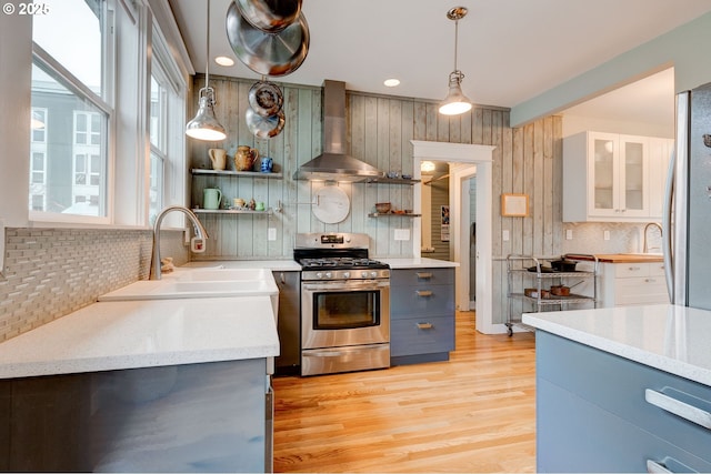 kitchen featuring a sink, light wood-style flooring, appliances with stainless steel finishes, wall chimney exhaust hood, and open shelves