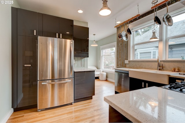 kitchen featuring backsplash, baseboards, light wood-style flooring, stainless steel appliances, and a sink