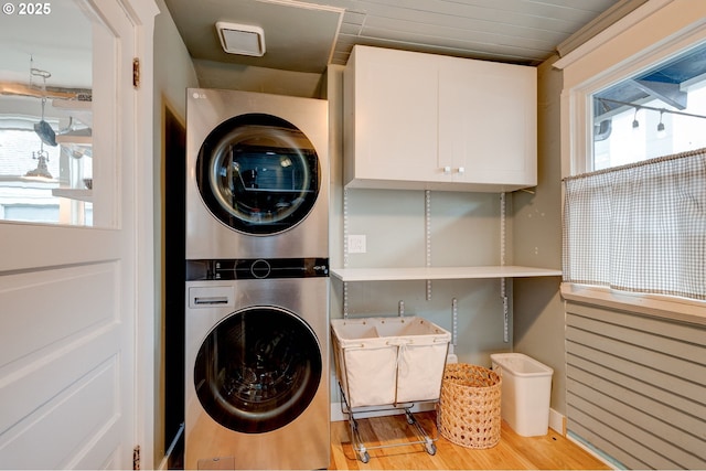 clothes washing area featuring cabinet space, wood finished floors, and stacked washer and clothes dryer