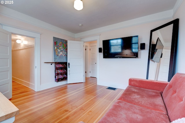 living room with visible vents, light wood-style flooring, baseboards, and ornamental molding