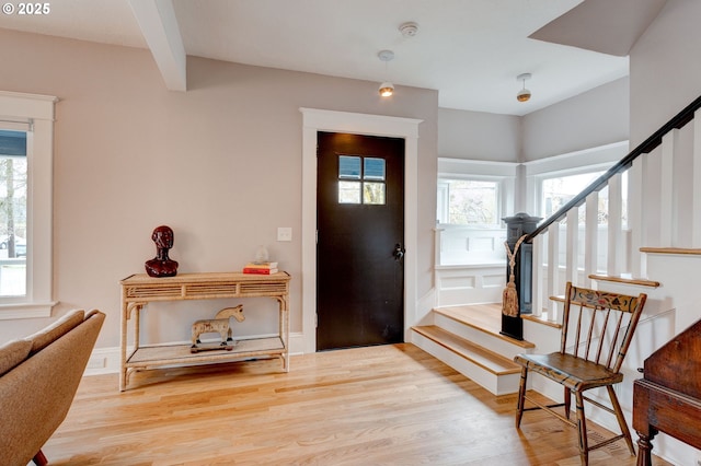 entryway with stairway, a healthy amount of sunlight, beamed ceiling, and light wood finished floors