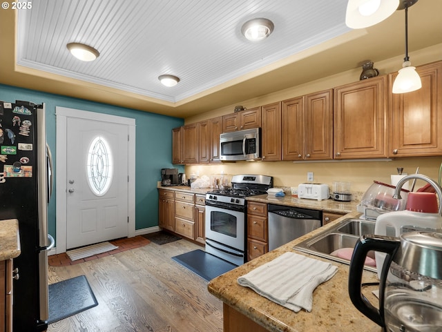 kitchen with brown cabinets, a sink, light wood-style flooring, appliances with stainless steel finishes, and decorative light fixtures