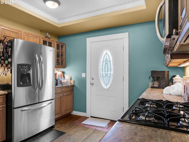 kitchen featuring brown cabinetry, crown molding, wood finished floors, stainless steel fridge with ice dispenser, and glass insert cabinets