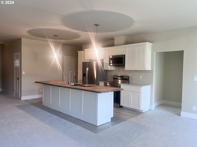 kitchen with hanging light fixtures, wooden counters, an island with sink, white cabinets, and appliances with stainless steel finishes