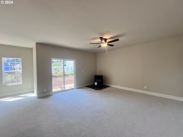 unfurnished living room with a wood stove, light carpet, and ceiling fan