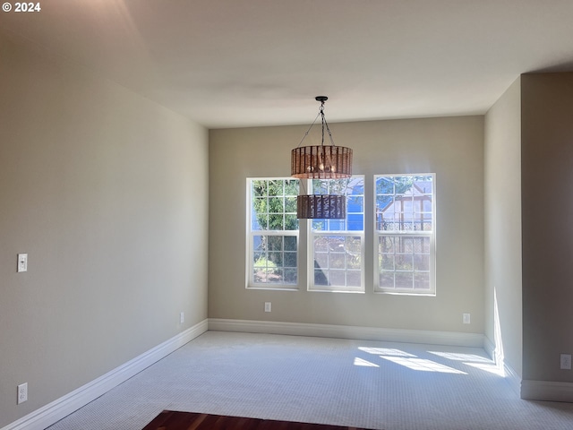 carpeted empty room featuring a notable chandelier