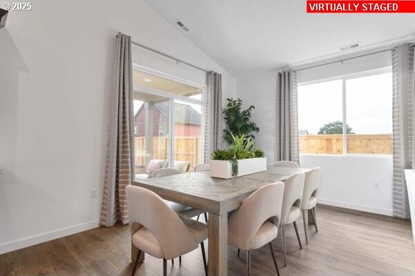 dining room featuring visible vents, baseboards, vaulted ceiling, and wood finished floors