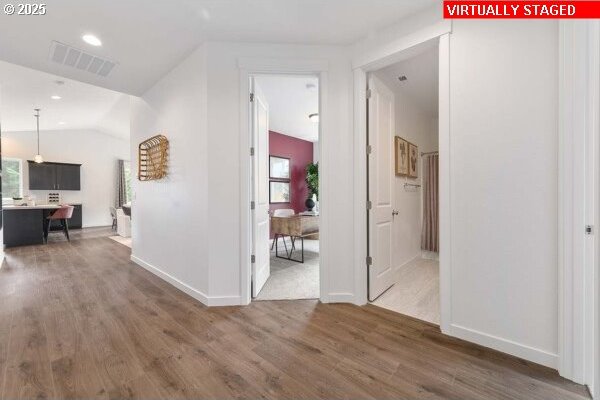 corridor with lofted ceiling, wood finished floors, visible vents, and baseboards