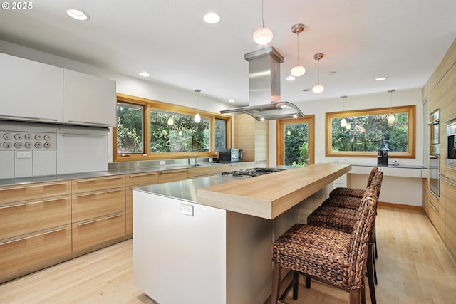 kitchen featuring island exhaust hood, modern cabinets, stainless steel counters, and stainless steel gas stovetop