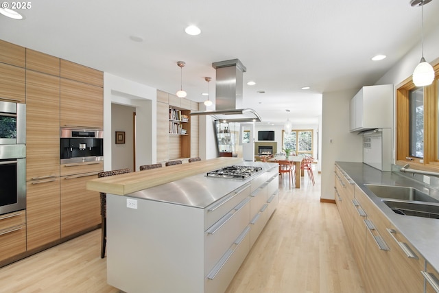 kitchen featuring stainless steel counters, a large island, modern cabinets, light wood-type flooring, and a sink
