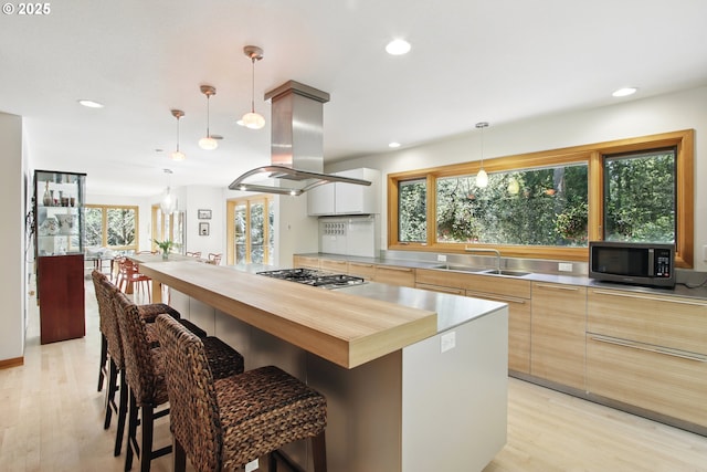 kitchen featuring modern cabinets, island range hood, light wood-type flooring, stainless steel countertops, and stainless steel appliances