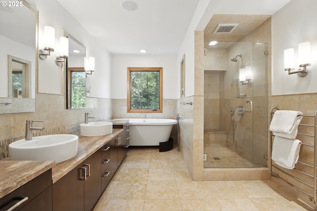 full bath with a sink, tile walls, a shower stall, and a freestanding tub