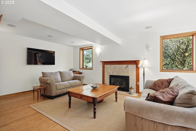 living area featuring baseboards, a tiled fireplace, a healthy amount of sunlight, and light wood finished floors