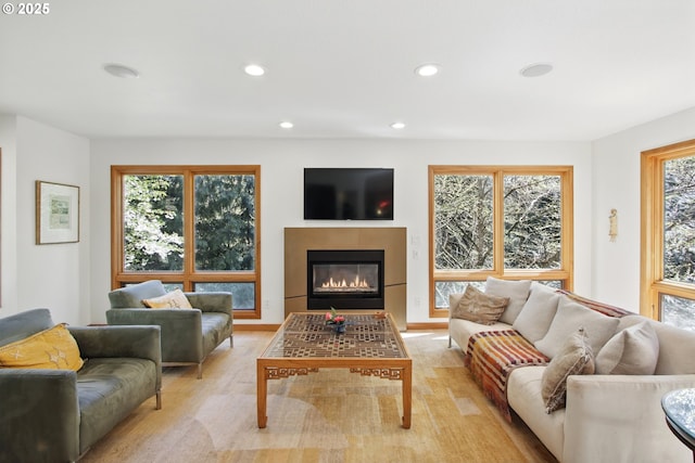 living area with recessed lighting, a glass covered fireplace, and light wood-type flooring