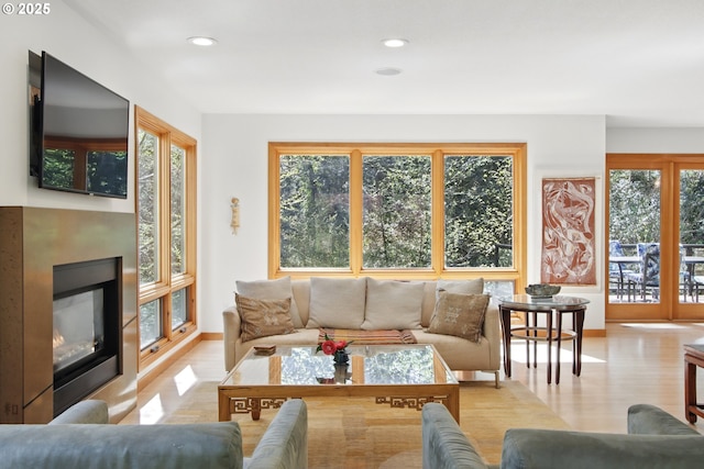 living area featuring a glass covered fireplace, recessed lighting, baseboards, and light wood-type flooring