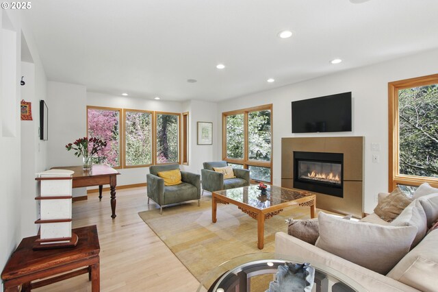 living room featuring recessed lighting, a tile fireplace, plenty of natural light, and light wood-style floors