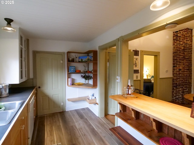 kitchen with open shelves, wood finished floors, wainscoting, white dishwasher, and a sink