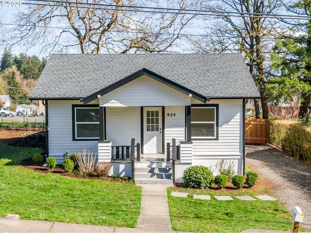 bungalow-style house with a front lawn, fence, roof with shingles, covered porch, and driveway