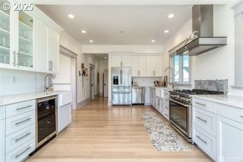 53139 Appleton Rd, Milton-Freewater, OR 97862 - kitchen featuring appliances with stainless steel finishes, wine cooler, wall chimney range hood, white cabinetry, and light wood finished floors