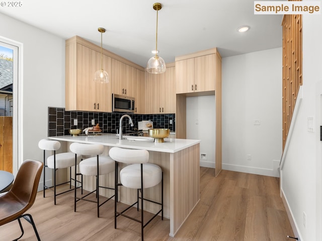 kitchen featuring a peninsula, tasteful backsplash, light brown cabinetry, stainless steel microwave, and light countertops