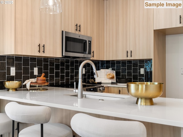 kitchen featuring a kitchen bar, stainless steel microwave, light brown cabinets, and backsplash