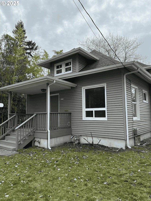 bungalow-style home featuring covered porch, roof with shingles, and a front yard