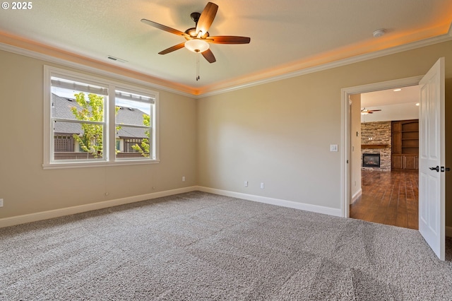 carpeted empty room featuring a ceiling fan, crown molding, a fireplace, baseboards, and a smoke detector