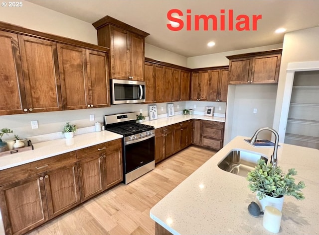 kitchen featuring light wood-style flooring, light stone countertops, stainless steel appliances, a sink, and recessed lighting