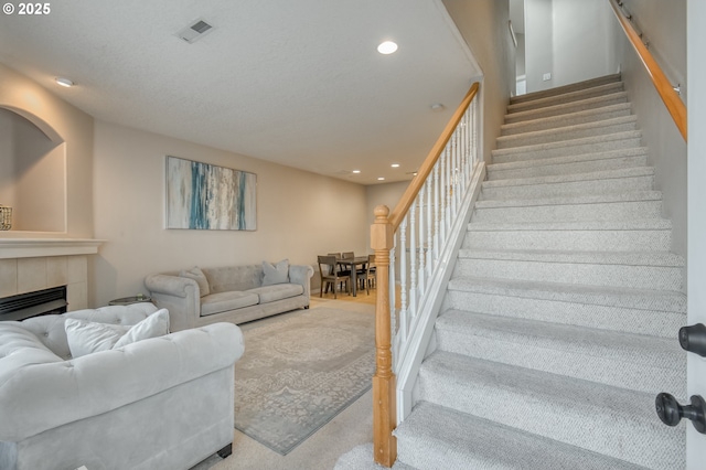 carpeted living room featuring stairway, visible vents, a tiled fireplace, and recessed lighting