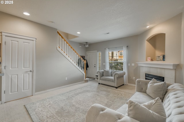 living room with carpet, recessed lighting, a tiled fireplace, baseboards, and stairs