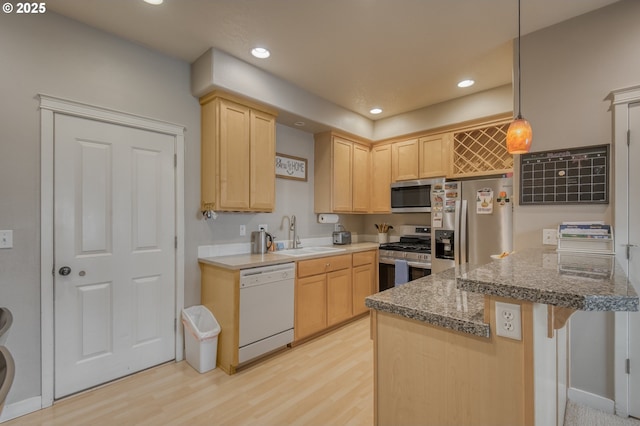 kitchen featuring light wood finished floors, appliances with stainless steel finishes, a peninsula, light brown cabinets, and a sink