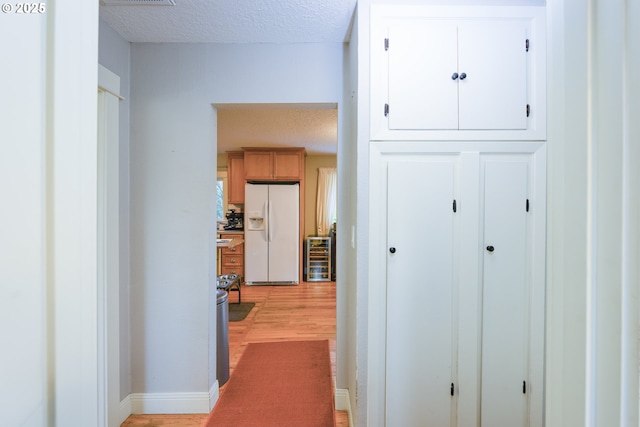 hallway with light hardwood / wood-style floors, beverage cooler, and a textured ceiling