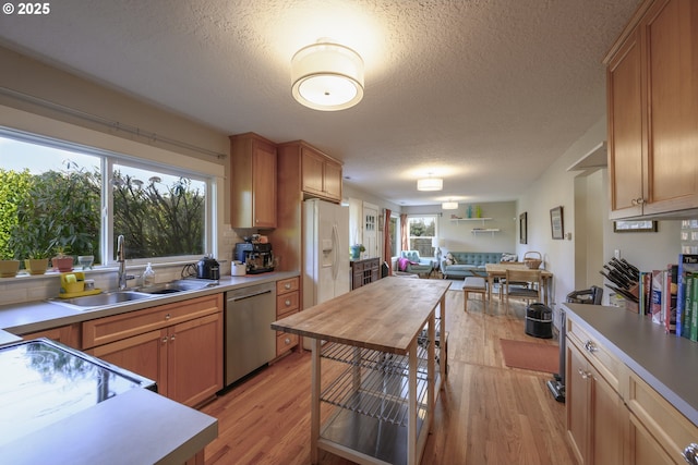 kitchen featuring sink, a textured ceiling, stainless steel dishwasher, white refrigerator with ice dispenser, and light hardwood / wood-style floors