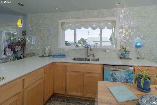 kitchen featuring tasteful backsplash, dishwasher, light countertops, a sink, and hanging light fixtures