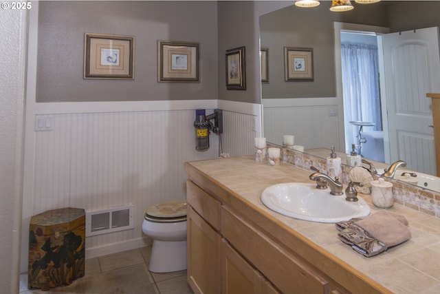 bathroom featuring visible vents, tile patterned floors, toilet, vanity, and a wainscoted wall