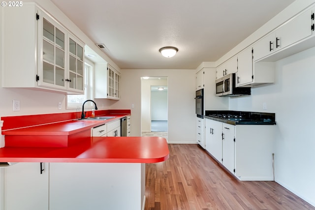 kitchen featuring light wood finished floors, visible vents, a peninsula, stainless steel appliances, and a sink