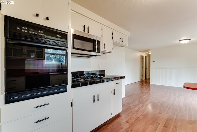 kitchen featuring tile countertops, light wood finished floors, black appliances, wainscoting, and white cabinetry