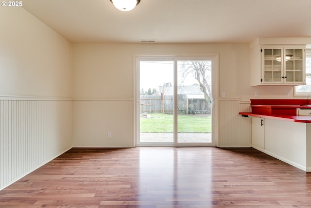 unfurnished dining area with a wainscoted wall, light wood-type flooring, and visible vents