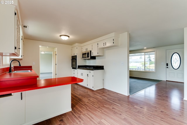 kitchen featuring a sink, stainless steel microwave, wood finished floors, and black oven