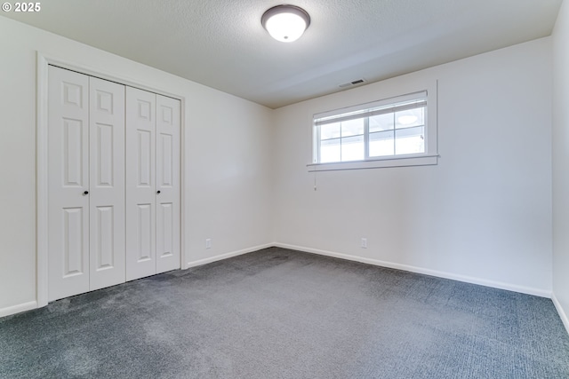 unfurnished bedroom featuring visible vents, a textured ceiling, a closet, dark colored carpet, and baseboards