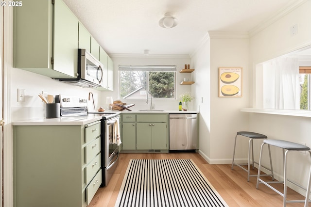 kitchen featuring green cabinets, light countertops, light wood-style flooring, appliances with stainless steel finishes, and a sink