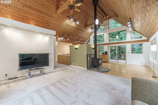 unfurnished living room with wood ceiling, high vaulted ceiling, a wood stove, carpet floors, and ceiling fan