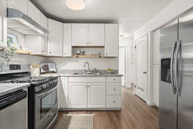 kitchen featuring appliances with stainless steel finishes, white cabinetry, sink, light stone countertops, and light hardwood / wood-style flooring