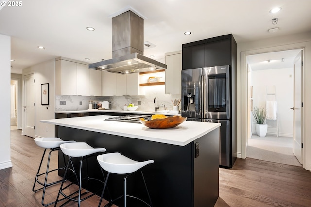 kitchen featuring a kitchen bar, island range hood, light hardwood / wood-style flooring, appliances with stainless steel finishes, and a kitchen island