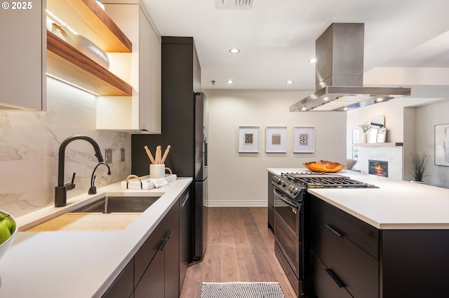 kitchen featuring sink, light wood-type flooring, island exhaust hood, black gas range, and backsplash