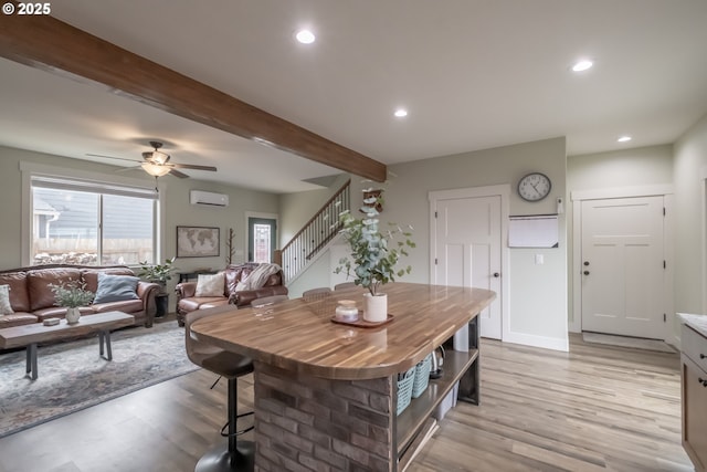 dining space with ceiling fan, a wall unit AC, beamed ceiling, and light wood-type flooring