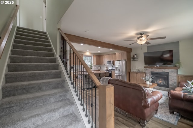 living room featuring light wood-type flooring, ceiling fan, and a stone fireplace