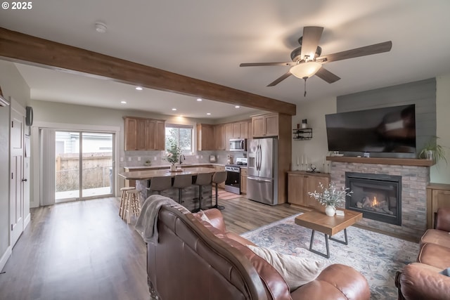 living room featuring ceiling fan, a fireplace, sink, beamed ceiling, and light hardwood / wood-style flooring